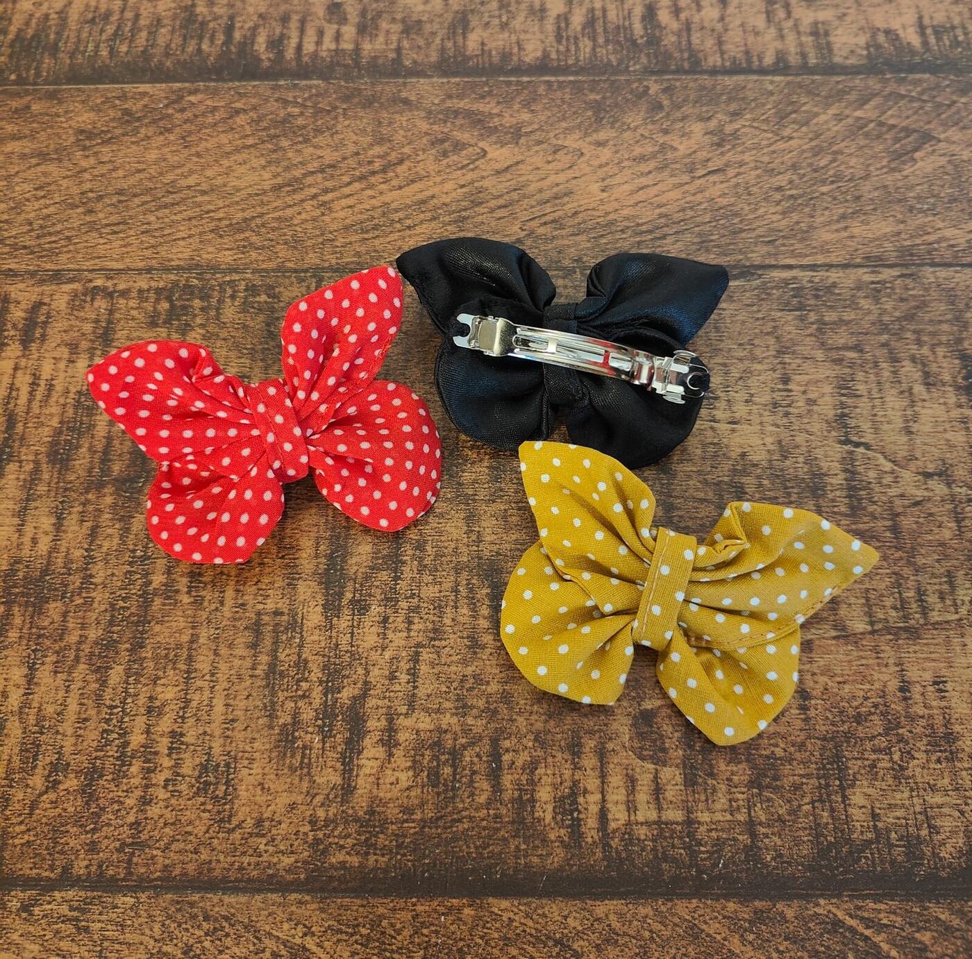 Trois barrettes en forme de nœud papillon : rouge à pois, noire, jaune à pois